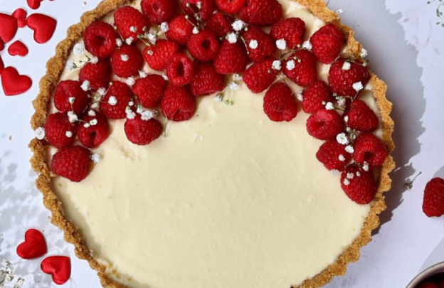 Image looking down on a white chocolate cheescake that is topped with bright red raspberries to one side