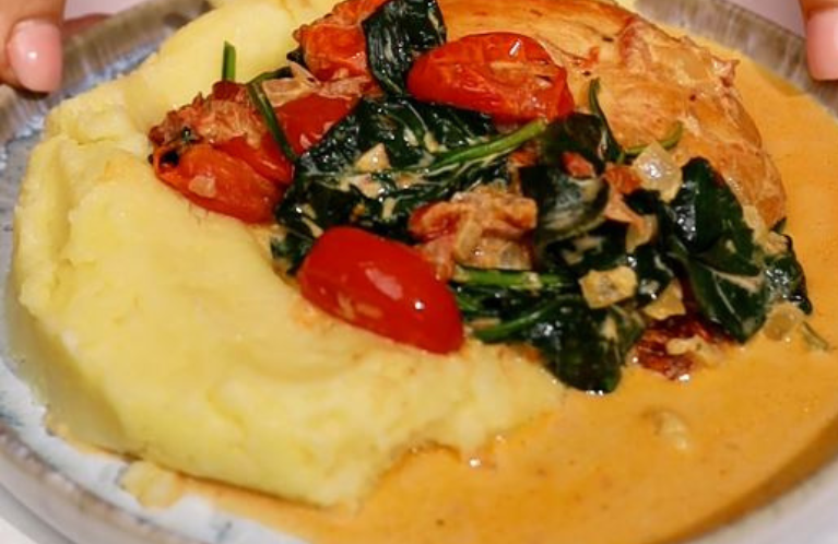 Plate with mashed potato on the bottom then layered with a breast of chicken with spinach and tomatoes