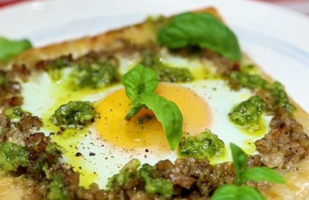 Image of a plate with puff pastry square with an egg in the middle with pesto drizzled on top