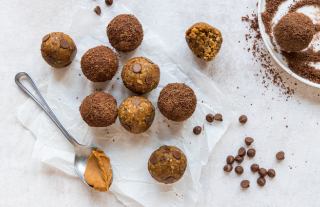 Snackballs in centre of image with spoon to the left hand side with peanut butter on it.